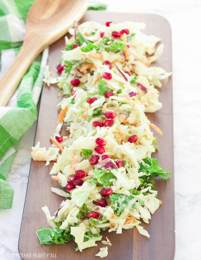 A healthy winter pomegranate cole slaw that's creamy and fresh and ready in under 5 minutes! The recipe uses a greek yogurt sauce as a base and then adds in apple slices, kale, lemon, and pomegranate to create a sweet and mellow sauce drizzled over crisp shredded cabbage and seasonal veggies.