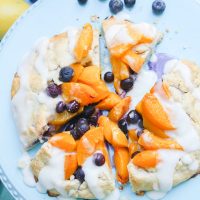 This peach blueberry galette combines peach slices and fresh blueberries in a sweet juicy sauce and then spreads it inside a doughy sugar-lined crust and bakes it all to golden perfection. This gluten free tart is drizzled in a light lemon glaze and is the perfect summer snack to enjoy outside on the back deck with a chilled bottle of white wine!