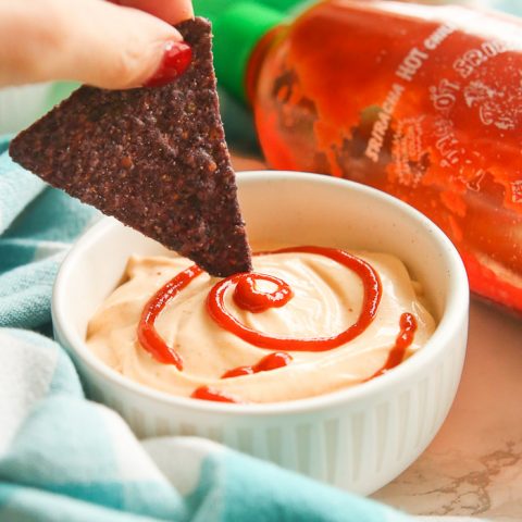 easy skinny sriracha aioli dip drizzle in green bowl dipping chip in sauce with fancy sriracha swirl