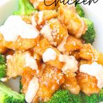 bang bang chicken is baked and not fried and is gluten-free with green broccoli florets in a white bowl with white creamy bang bang sauce drizzled on top