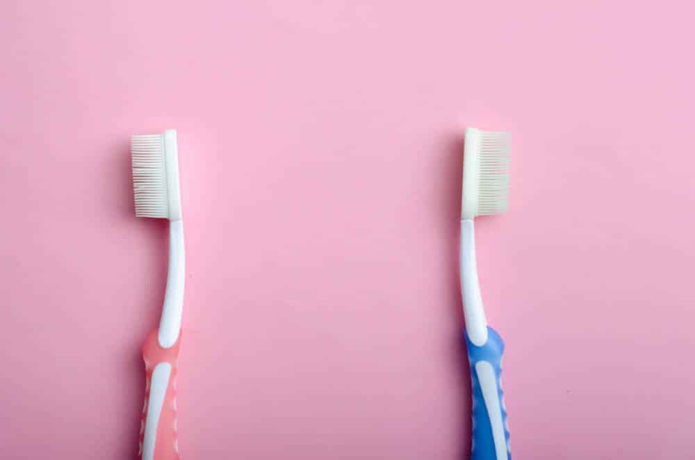 Two Toothbrushes Facing apart from one another, pink background