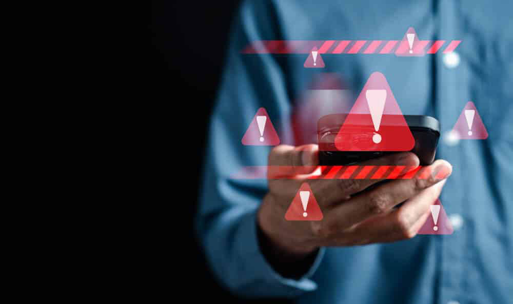 Man holding phone, red warning signs all around, blue shirt, black background