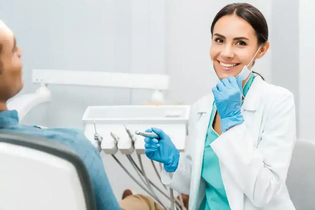 Female Dentist smiling looking at the camera. Patient seen in frame getting treatment.