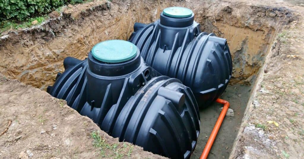 Two plastic black underground septic tanks sit inside an uncovered square hole dug into the ground.