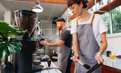 crop baristas against coffee maker and grinder in cafe kitchen