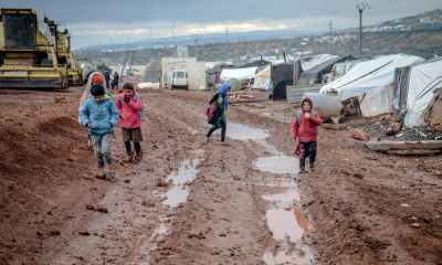 poor children walking on muddy ground in settlement with tents