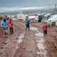 poor children walking on muddy ground in settlement with tents