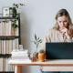 pensive woman browsing laptop near books