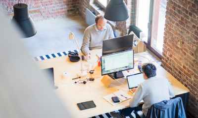 two men sitting facing on flat screen monitors