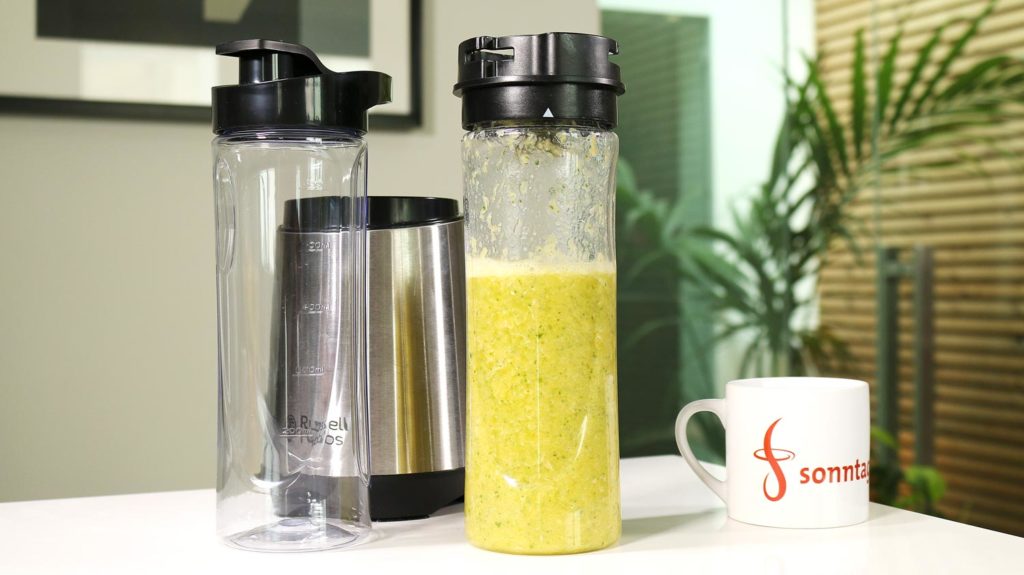 Russell Hobbs Mix & Go Steel - Standfuss mit beiden Mixbehältern im Vordergrund, der rechts stehende ist mit frisch zubereitetem Smoothie gefüllt