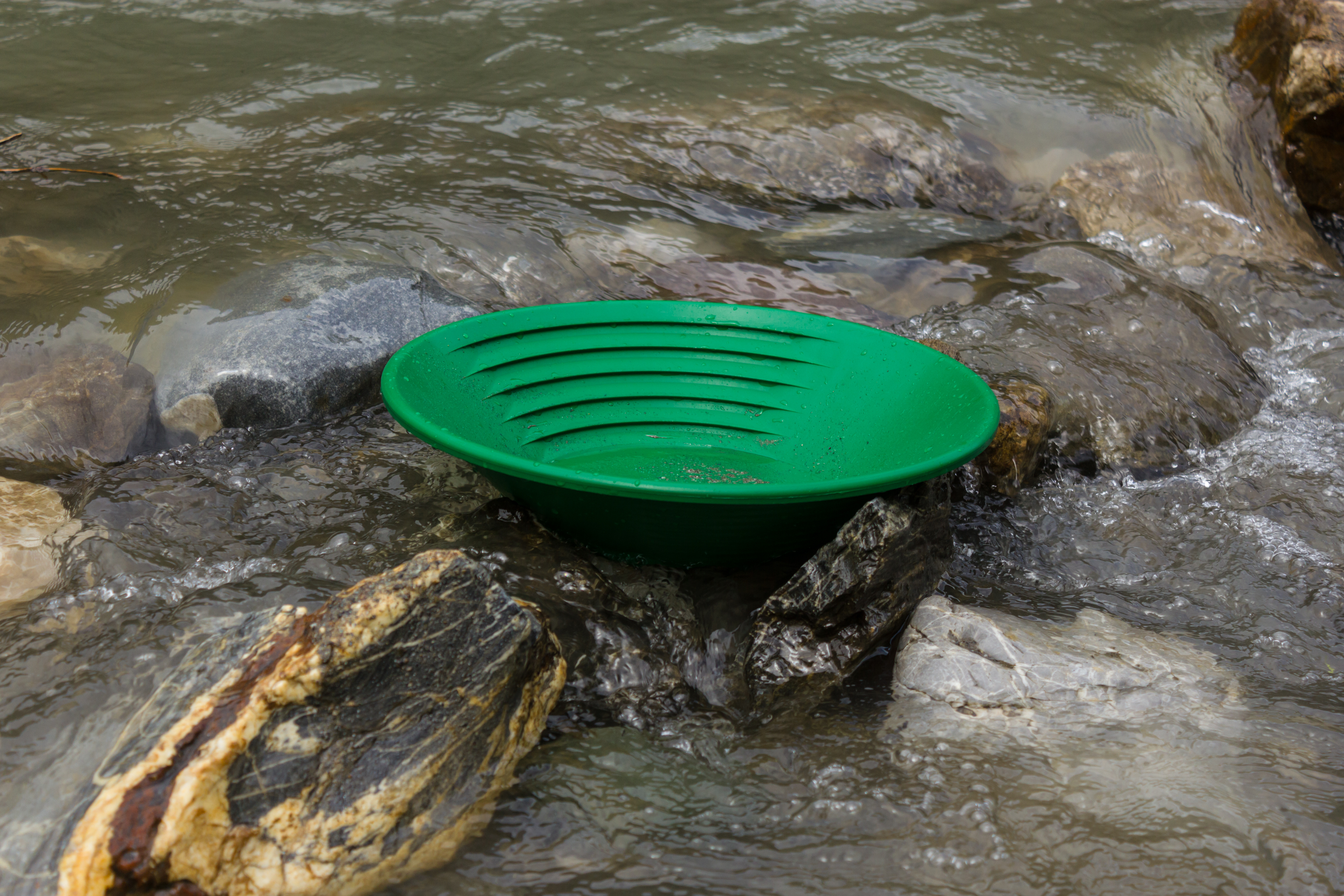Effective Gold Pan Usage: Double Your Recovery with These Secret Moves A green plastic gold panning pan sits on rocks in a shallow, flowing stream, demonstrating effective gold pan usage for prospectors seeking treasure.