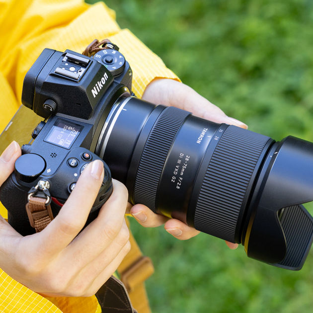 Person holding a Nikon camera with a mounted Tamron 28-75mm f/2-2.8 lens, outdoors with a green blurred background.