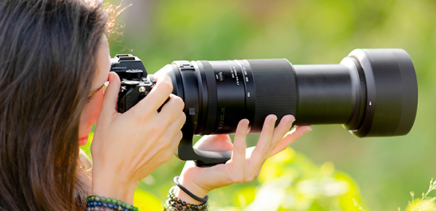 Photographer with camera using a long telephoto lens outdoors in natural light with a green background.