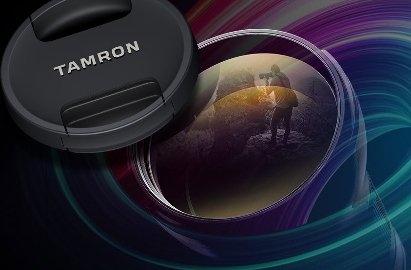 Close-up of a Tamron lens with cap and reflection of a photographer in the glass, set against a colorful abstract background.