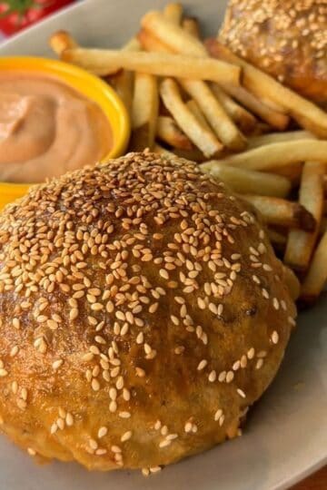 Rice Paper Cheeseburger Wellington with sesame seed bun, fries, and dipping sauce on a white plate.