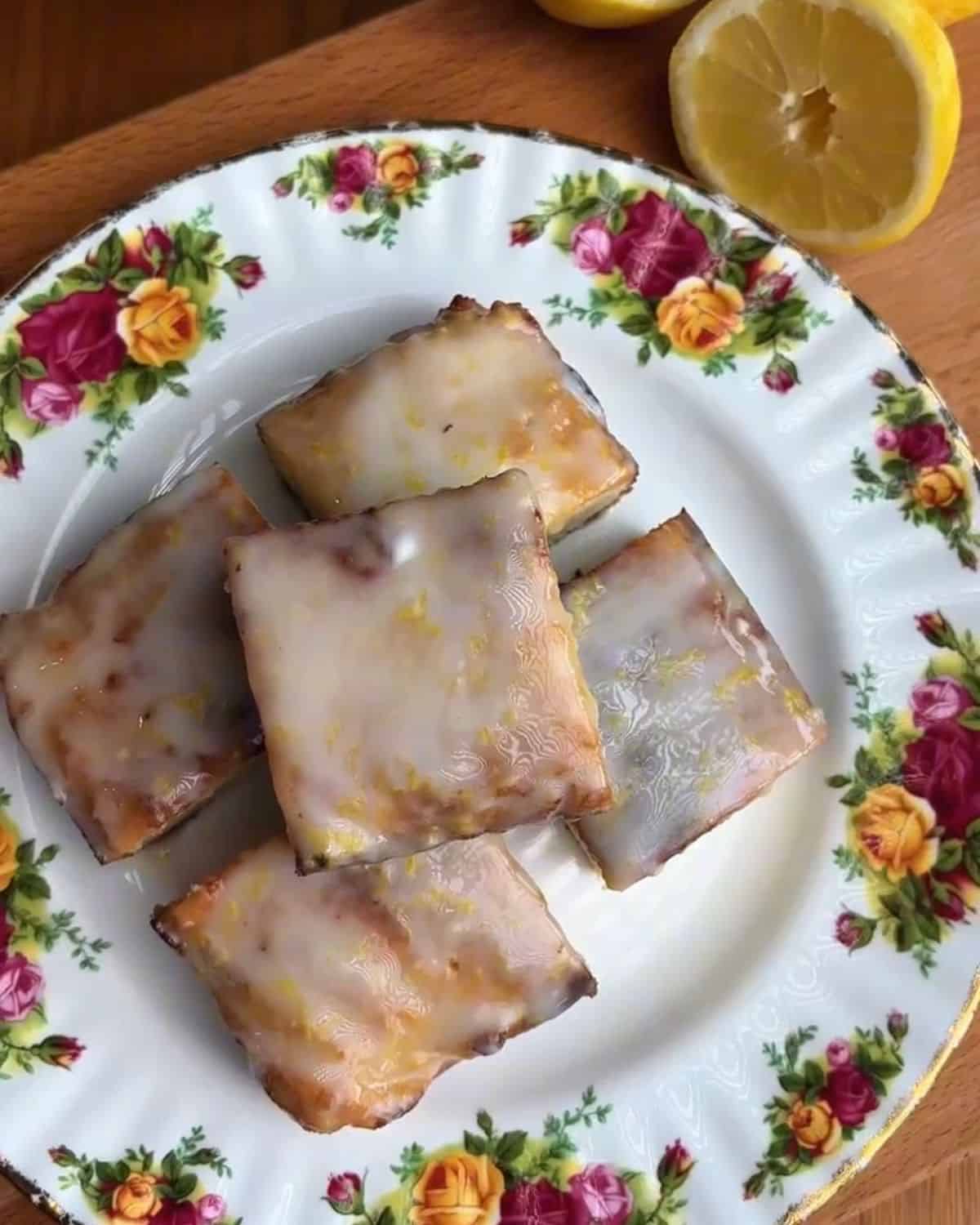 Delicious lemon-glazed bars served on a floral plate with lemon halves.