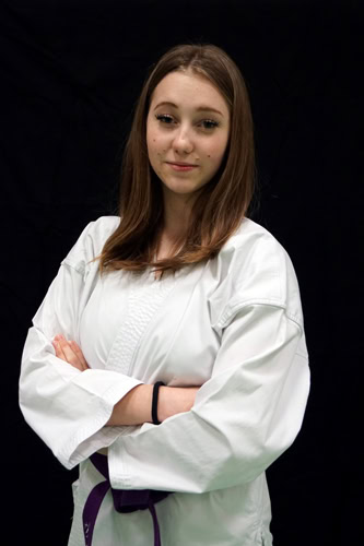 Frau in weißem Karateanzug mit lila Gürtel.
