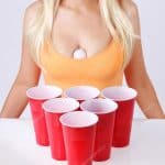 Beer pong. Red plastic cups with ping pong ball and blonde girl in sexy tank top.