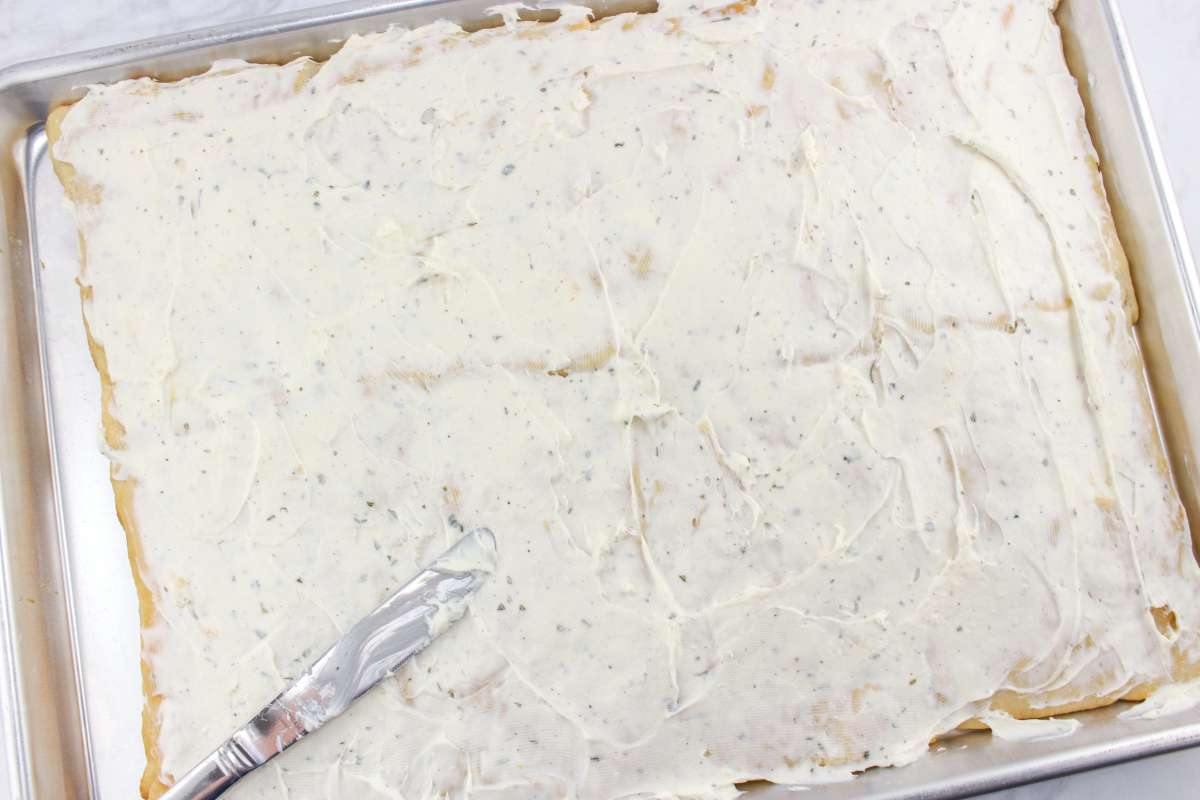 Spreading cream cheese mixture over crescent rolls dough.