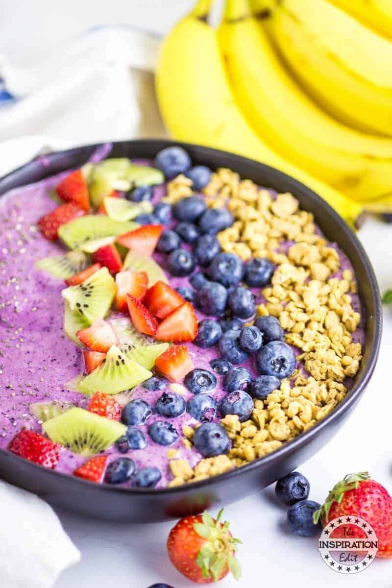 Purple smoothie in bowl topped with blueberries, strawberries, kiwi, and granola. 