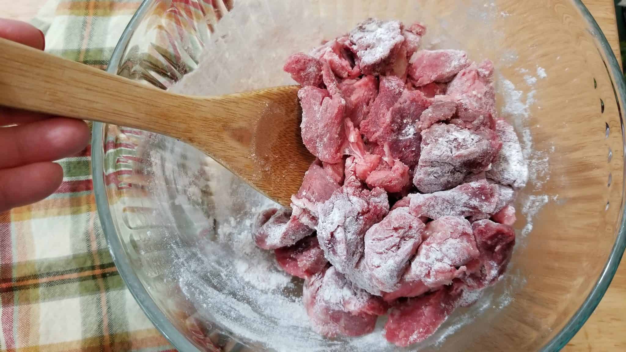 Coating uncooked beef with flour.