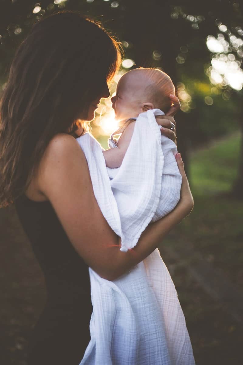 Mother holding baby with sun shining behind them.