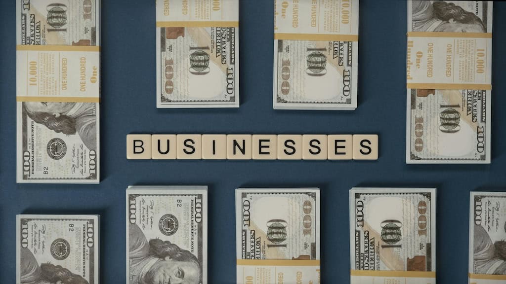 Stacks of U.S. Hundred-Dollar Bills with the Word 'BUSINESSES' in Scrabble Tiles.