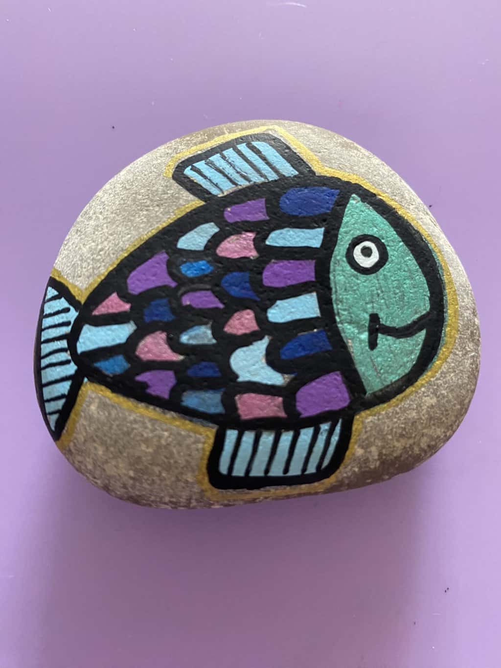a smiling fish painted rock with fins and scales. 