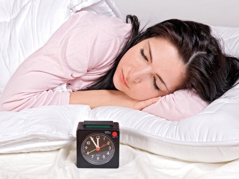 Sleep Is The Key To A Healthier Life | Woman sleeping with an Alarm Clock in front of her.