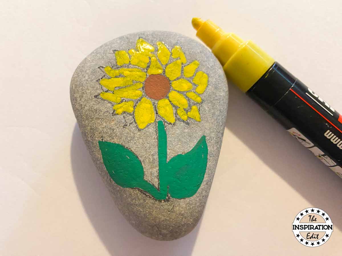 adding yellow paint to sunflower painted rock. 