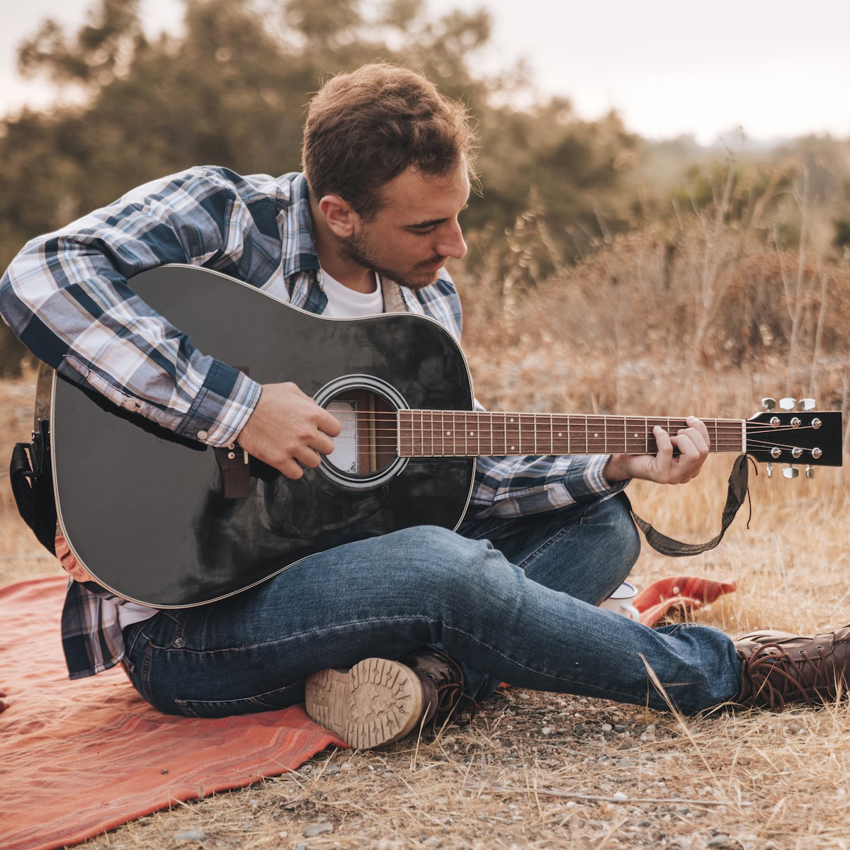 Learning to Play The Guitar | man sitting blanket playing guitar.