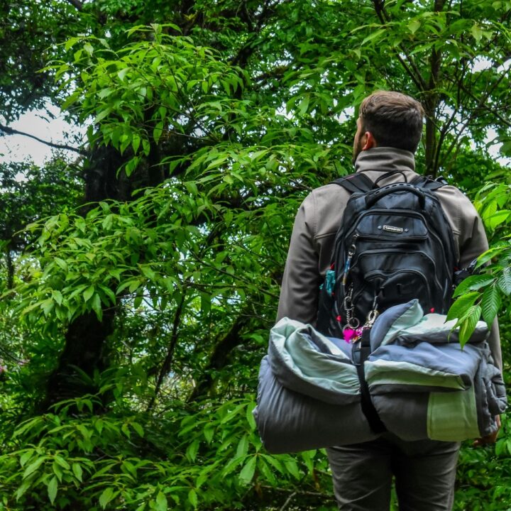 Items That Belong in Every Camper’s Bag | A camper with a backpack on, full of camping gear.