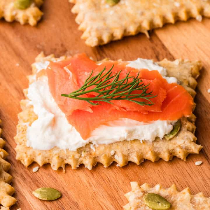 Einkorn Maple Crackers with cream cheese, salmon and dill on a wooden chopping board.