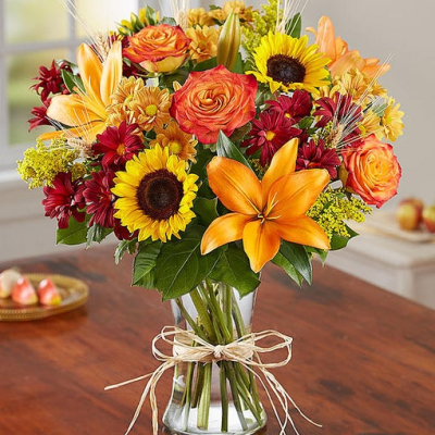 Inspired by the colorful charm of the European countryside, our best-selling autumn bouquet is gathered with fresh-picked flowers, revealing the rustic beauty of nature. Shades of golden yellow, rich red and pops of orange create a timeless gift for someone special to enjoy. All-around arrangement with autumn-colored roses, sunflowers, orange Asiatic lilies, red and autumn-colored daisy poms; accented with wheat, solidago and assorted greenery Artistically designed in a clear glass vase accented with raffia