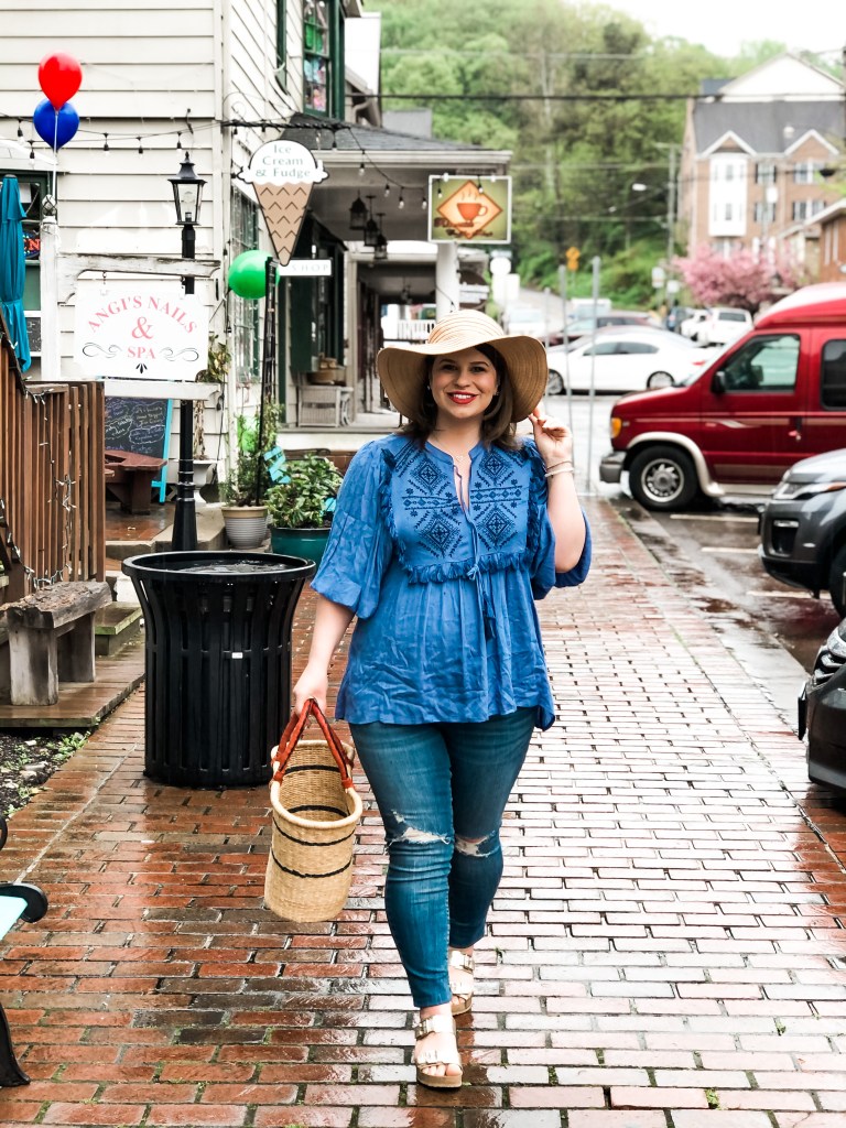 woman walking on the streets wearing a hat, blue top, and jeans 