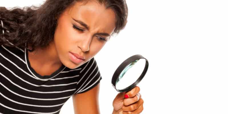 Beautiful young dark skinned woman looking trough the magnifying glass