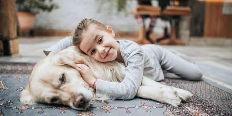Cute little girl relaxing with her dog on carpet at home