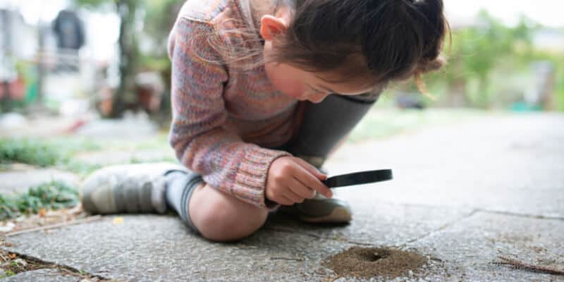 Girl observing ant nest with magnifying glass