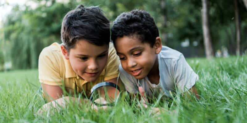 selective focus of multicultural boys lying on grass and looking through magnifier