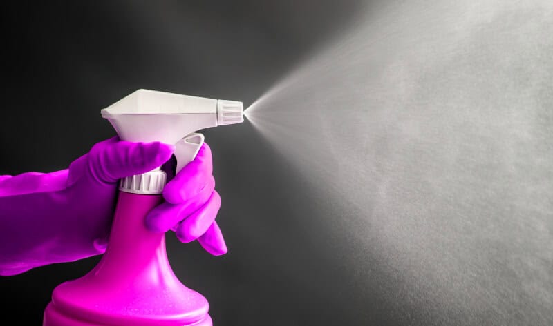 Woman wearing pink rubber gloves using pink spray bottle and spraying 
 white vinegar in air