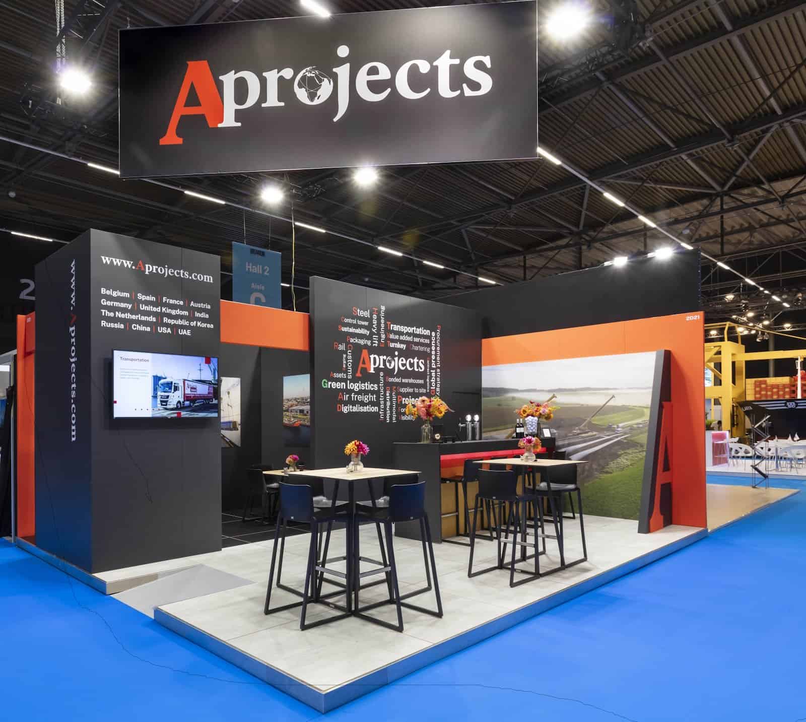 Overzicht van de zakelijke beursstand voor A Projects op Breakbulk, met een zwarte achterwand, oranje accenten en diverse zitjes.