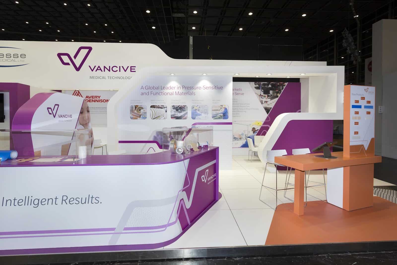 De centrale ontvangstbalie van de Avery Dennison stand, met de Vancive Medical Technology branding en productdisplays.