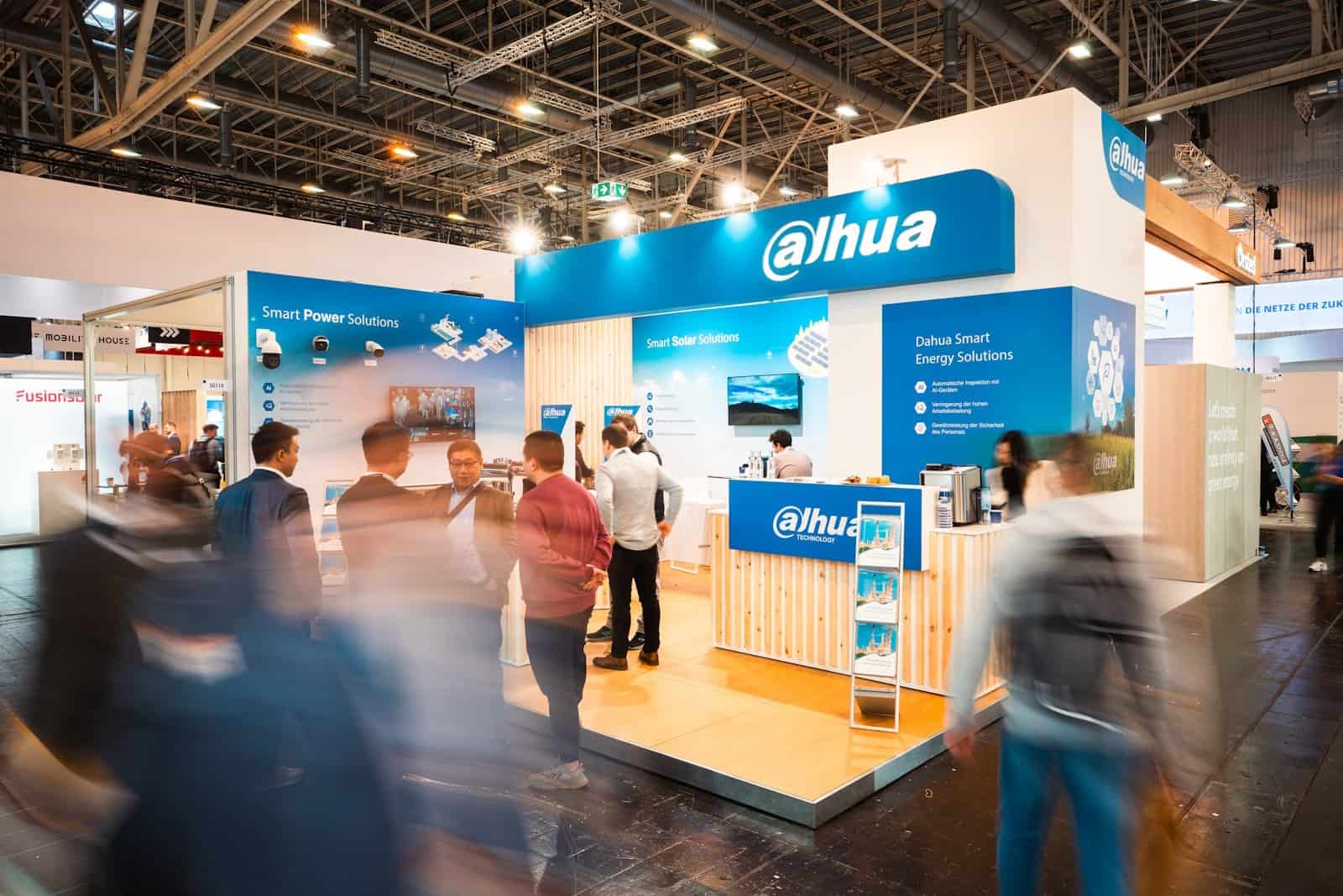 Drukbezochte beursstand voor Dahua Technology in blauw en wit, met bezoekers die interageren met het personeel en de demo-opstellingen.