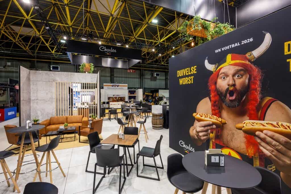 Detail van de branding-wanden met een grote, humoristische visual ("Haast, dat zal ons een worst wezen") en een visual van Pure Ambacht op de stand van Charles.