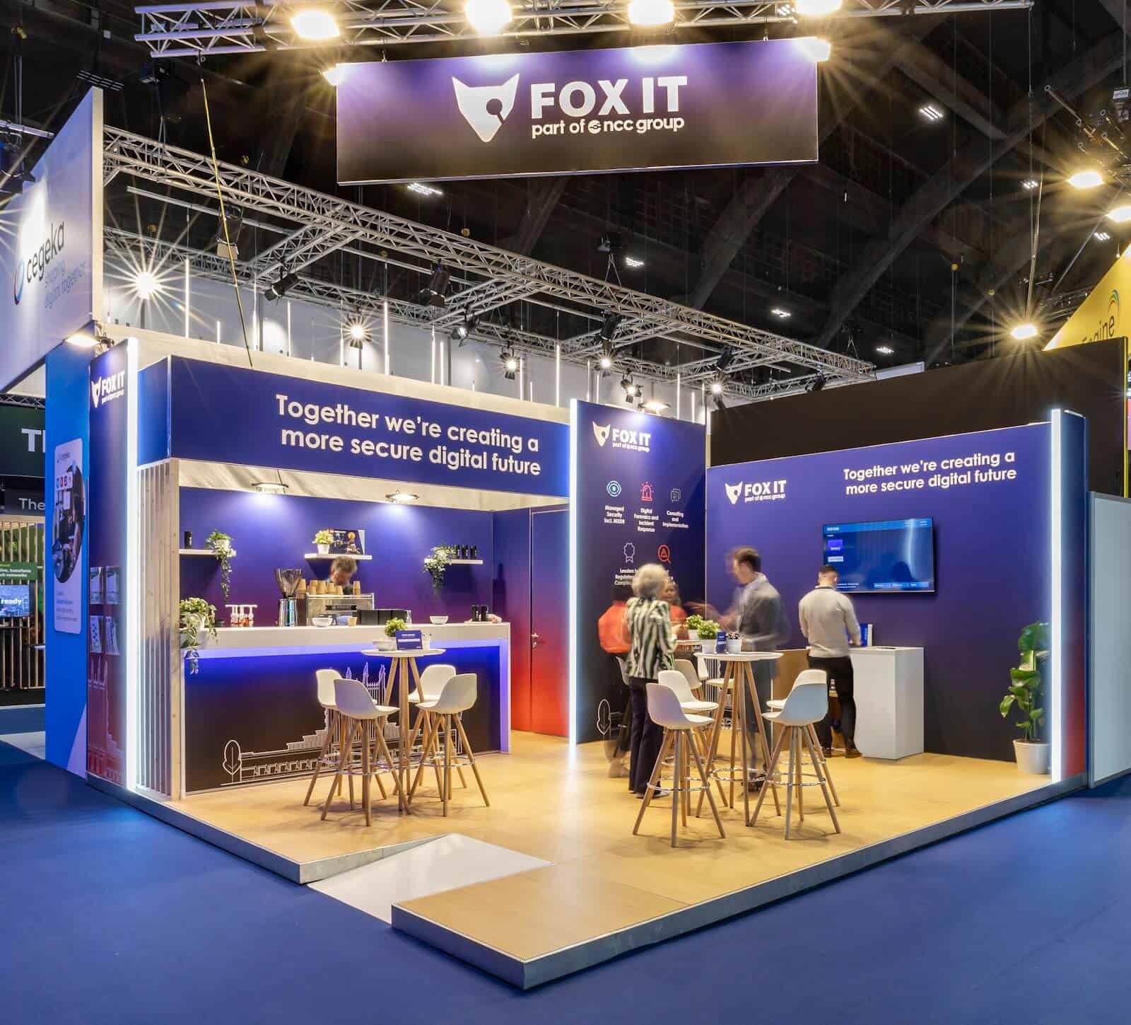 Overzicht van de minimalistische beursstand van Fox-IT, ontworpen als een architecturale 'box' met een strakke, witte binnenkant en een donkere buitenkant.