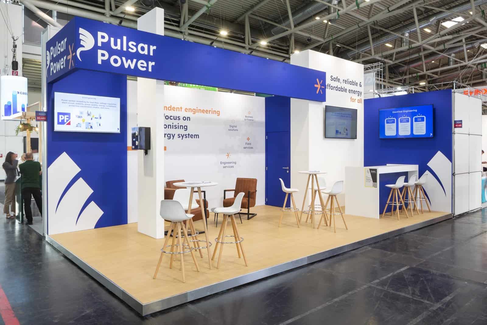 Overzicht van de professionele beursstand voor Pulsar Power in blauw en wit, met diverse zitjes en een grote luifel.