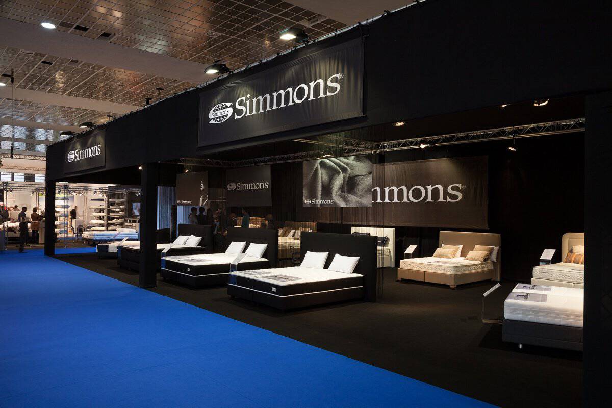 De collectie luxe matrassen en bedden van Simmons bedding, sfeervol uitgelicht met spots in een donkere en chique showroom-omgeving.