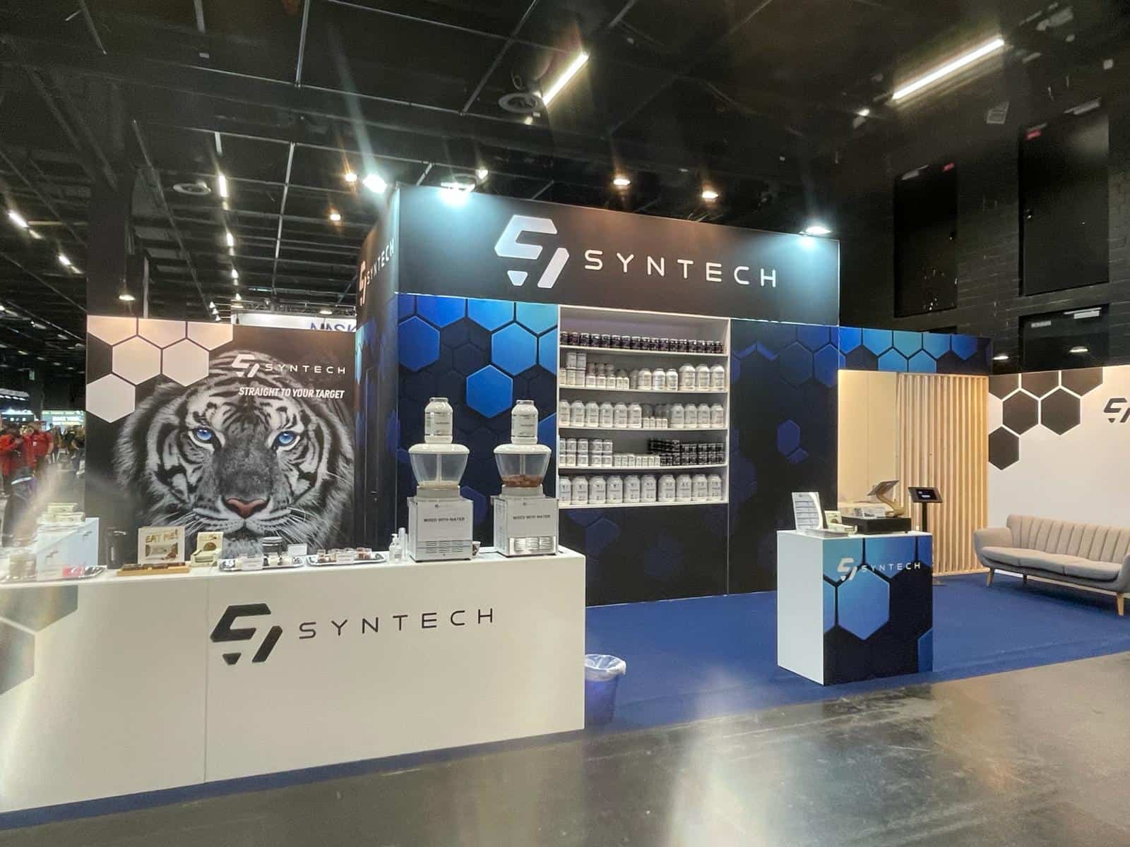 ooraanzicht van de Syntech beursstand, met een grote, opvallende visual van een tijger naast de tasting bar en de productwand.