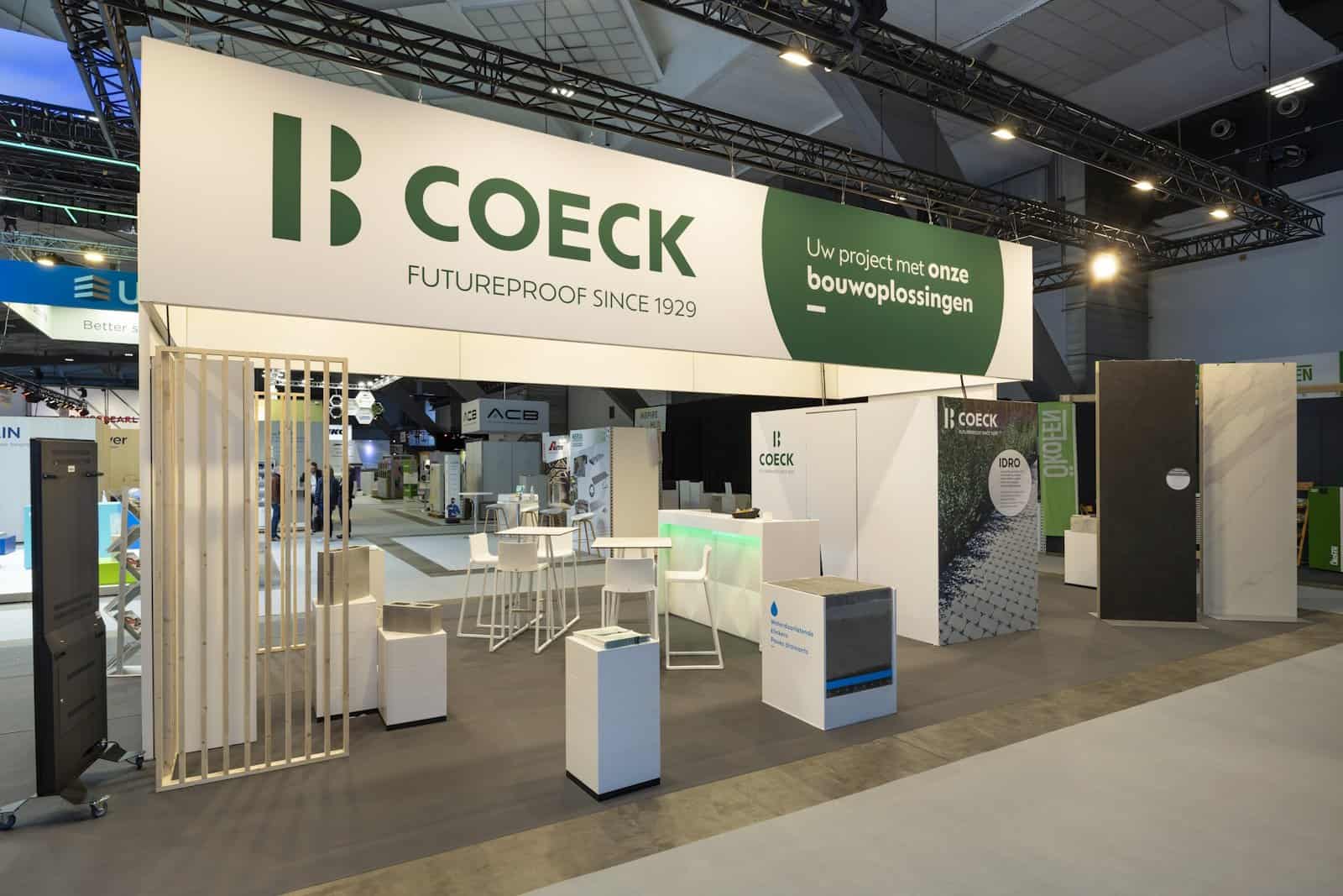 Vooraanzicht van de Coeck beursstand met de gastvrije ontvangstzone, een witte bar en prominente branding.