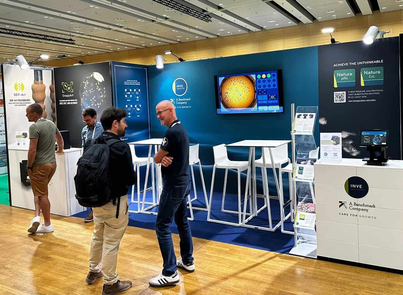 Overzicht van de compacte beursstand voor INVE Aquaculture, die een informatieve wand combineert met een open en functionele inrichting.